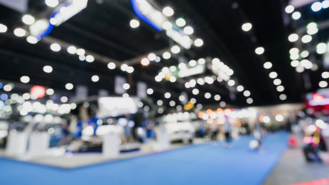 Blurred, defocused background of public event exhibition hall showing cars and automobiles, business commercial event concept